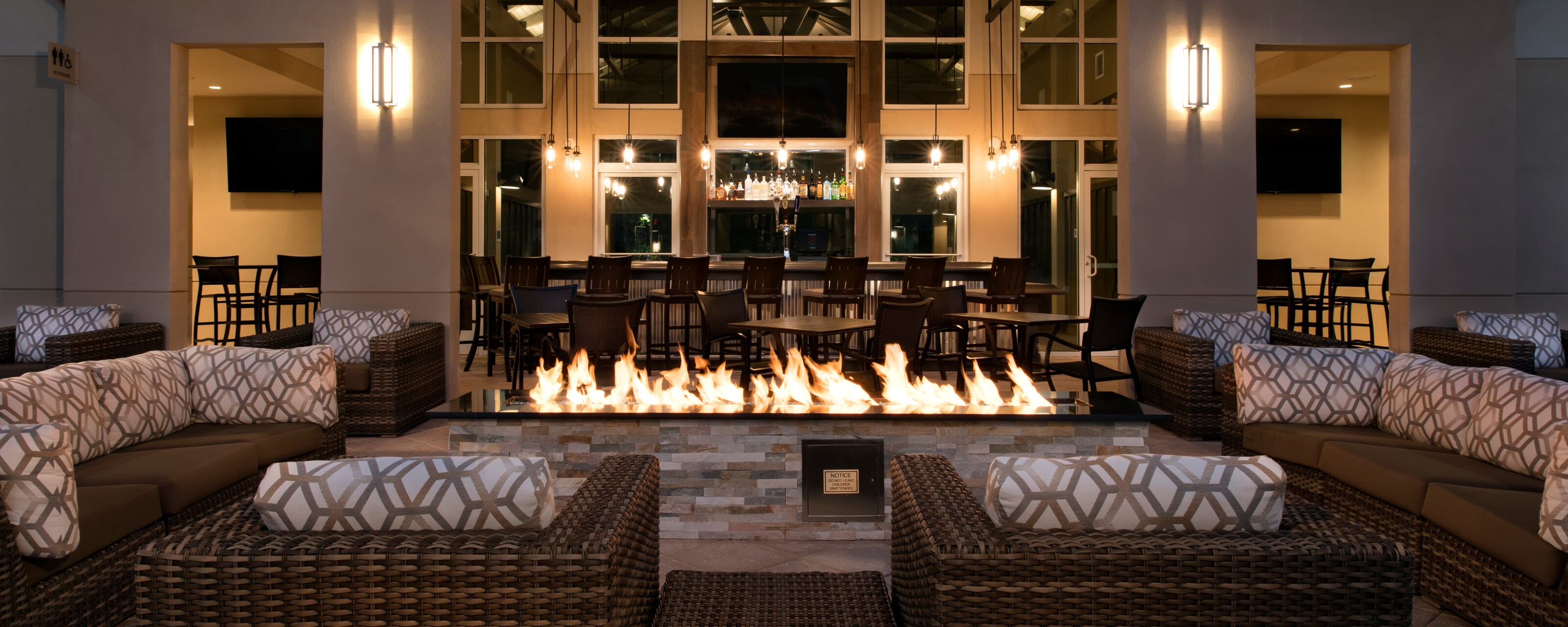 Rattan sectional sofas around a large firepit, with a bar in the background