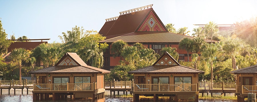 Three bungalows along the water with palm trees in the background