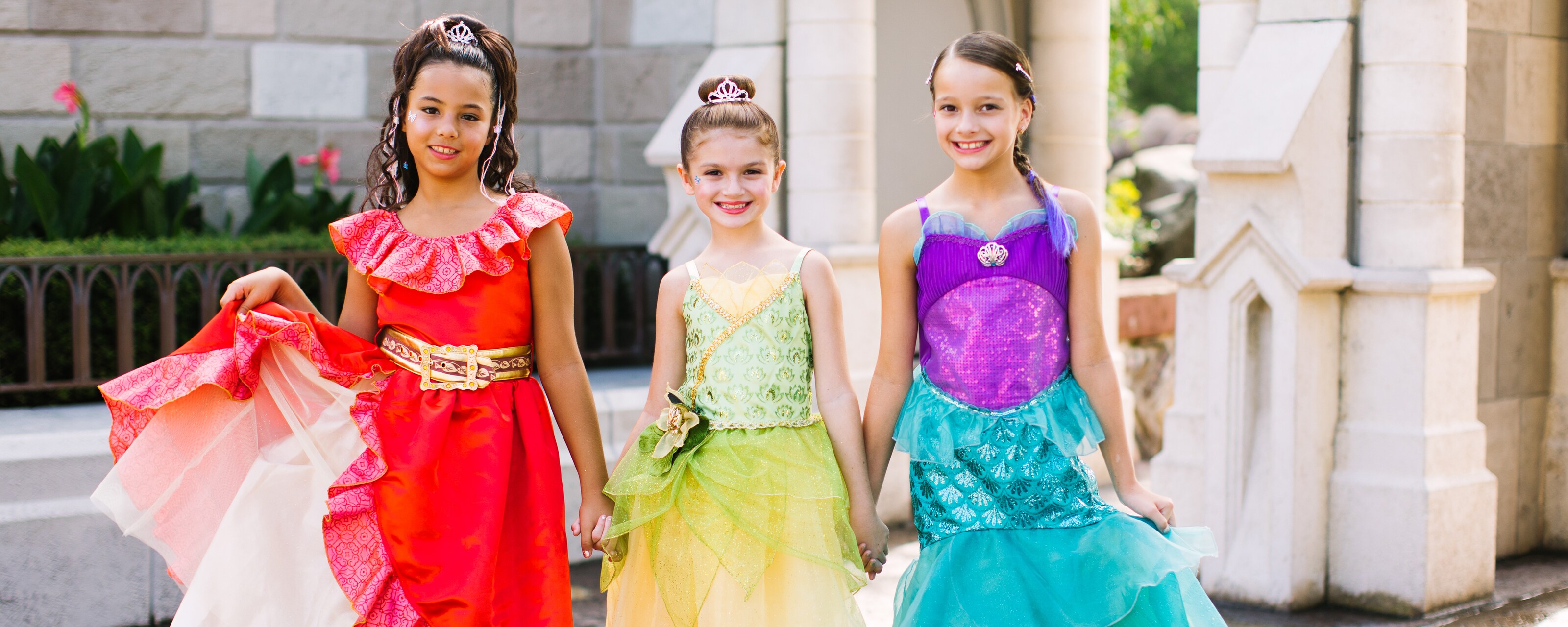 3 girls in princess dresses and fancy shoes pose in front of Cinderella Castle