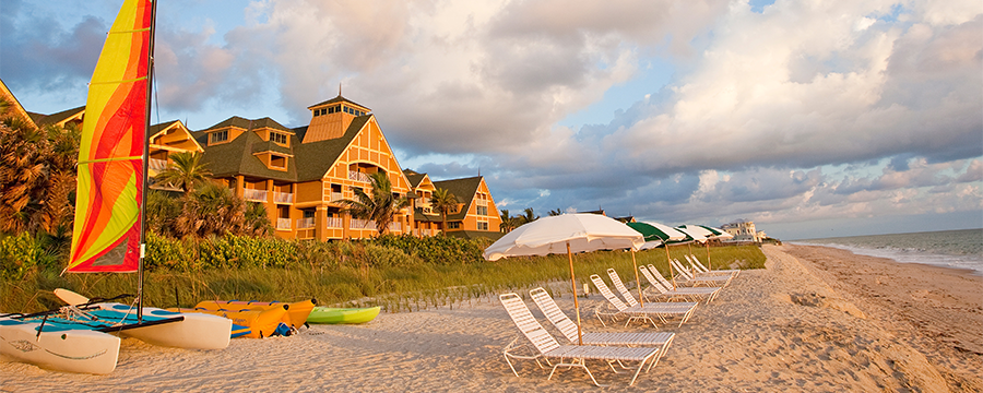 A beach with lounge chairs, umbrellas and rental boats, and the Resort behind