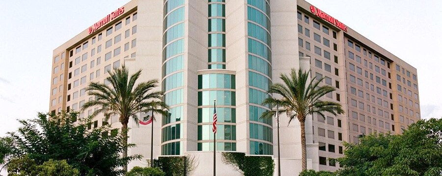 The exterior of the Anaheim Marriott Suites with 2 palm trees and the American flag in front of the main entrance
