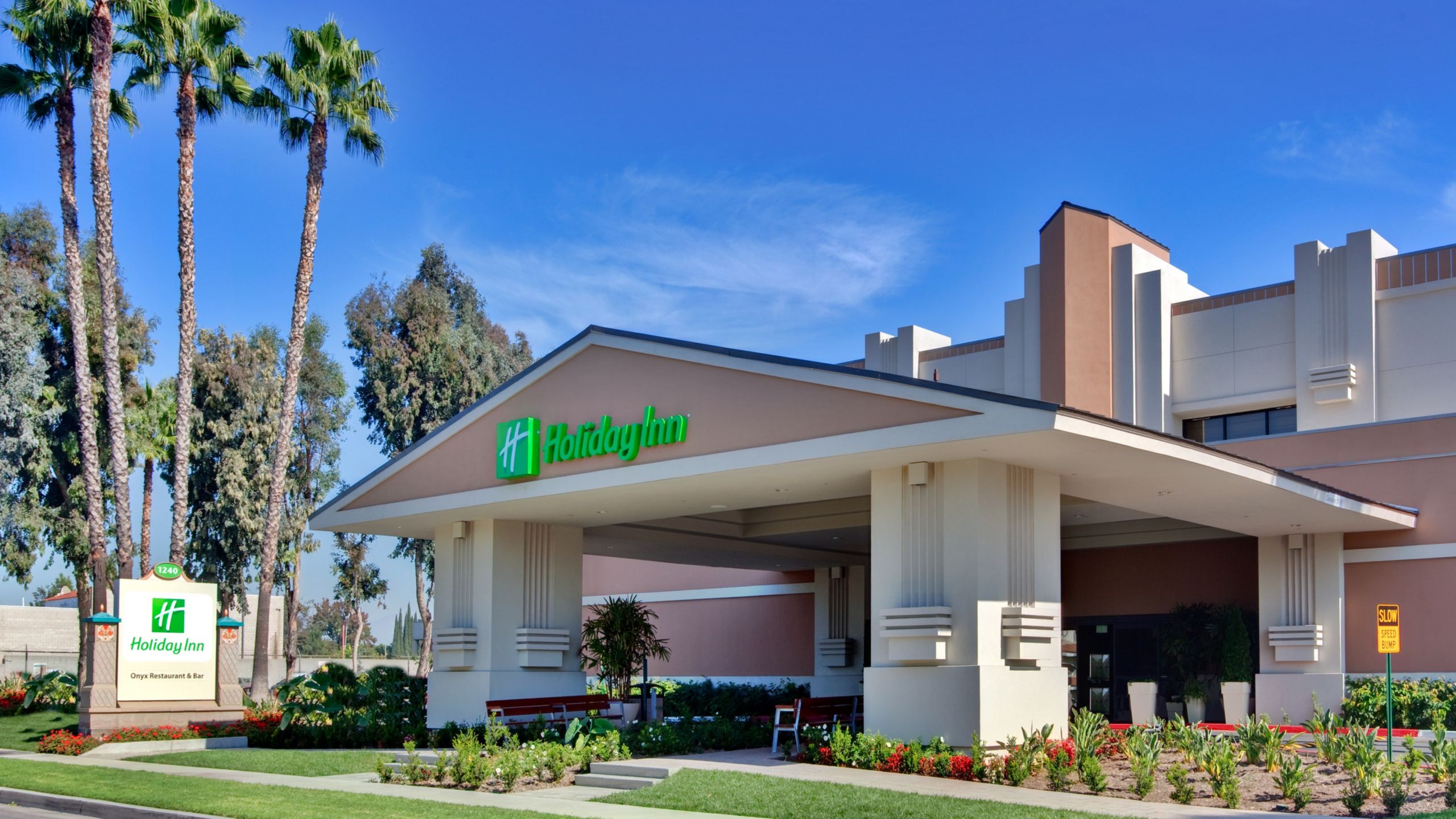 The exterior of Holiday Inn & Suites Anaheim with a covered driveway, palm trees and other plants