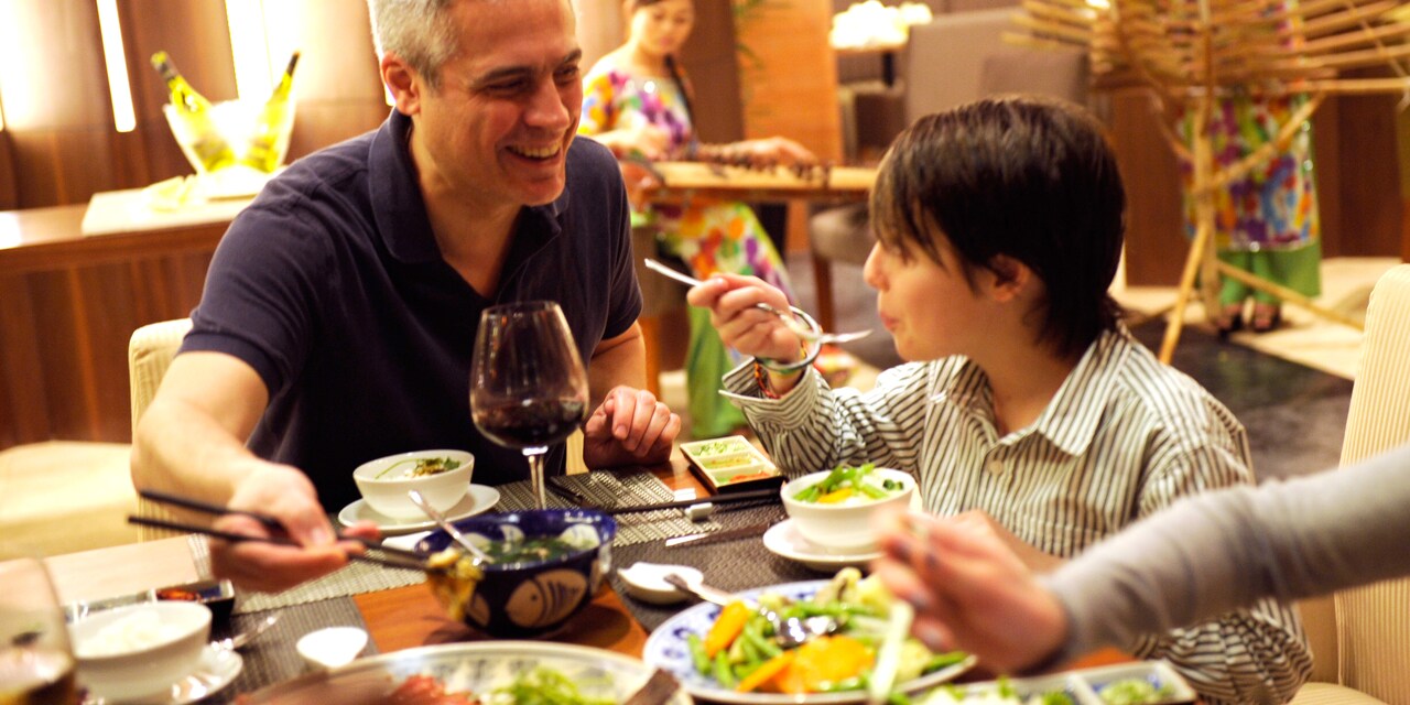 A boy blows on his hot soup to cool it as his father eats from a bowl with chopsticks
A boy blows on his hot soup to cool it as his father eats from a bowl with chopsticks