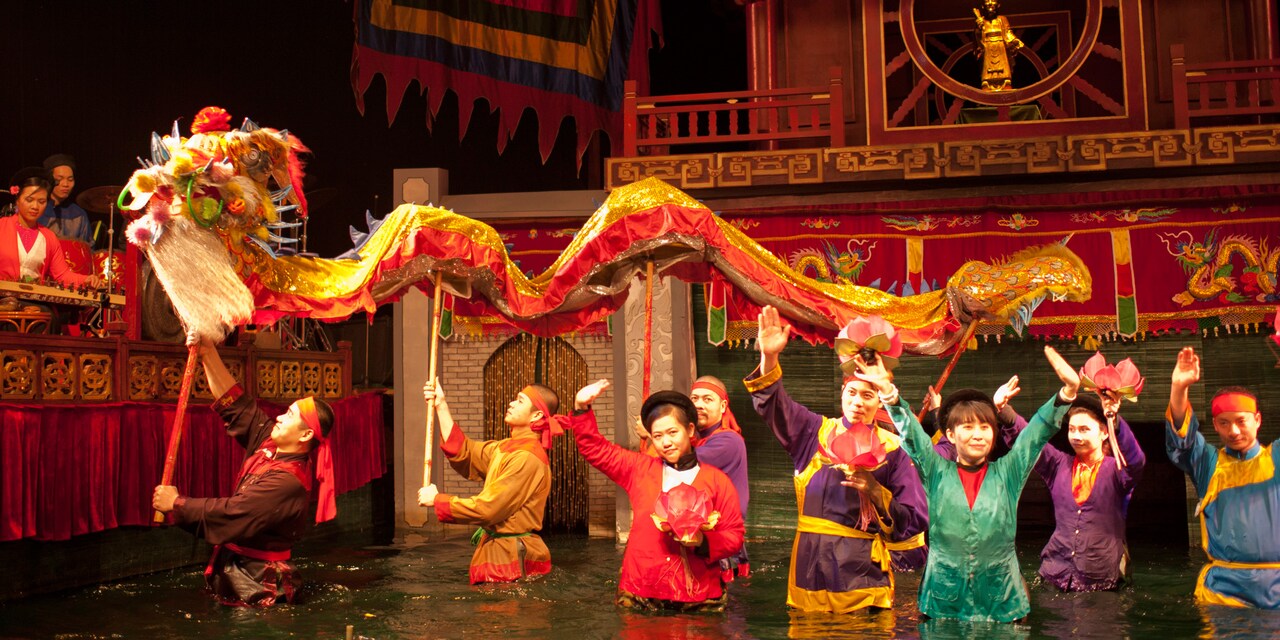 Costumed performers walk through a river carrying a long dragon puppet Costumed performers walk through a river carrying a long dragon puppet