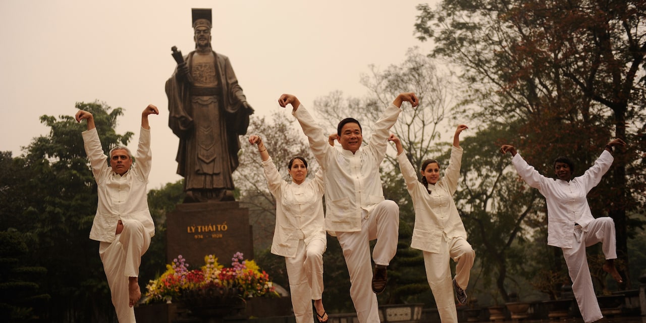 People raise their arms and one of their legs in an outdoor Tai Chi class People raise their arms and one of their legs in an outdoor Tai Chi class