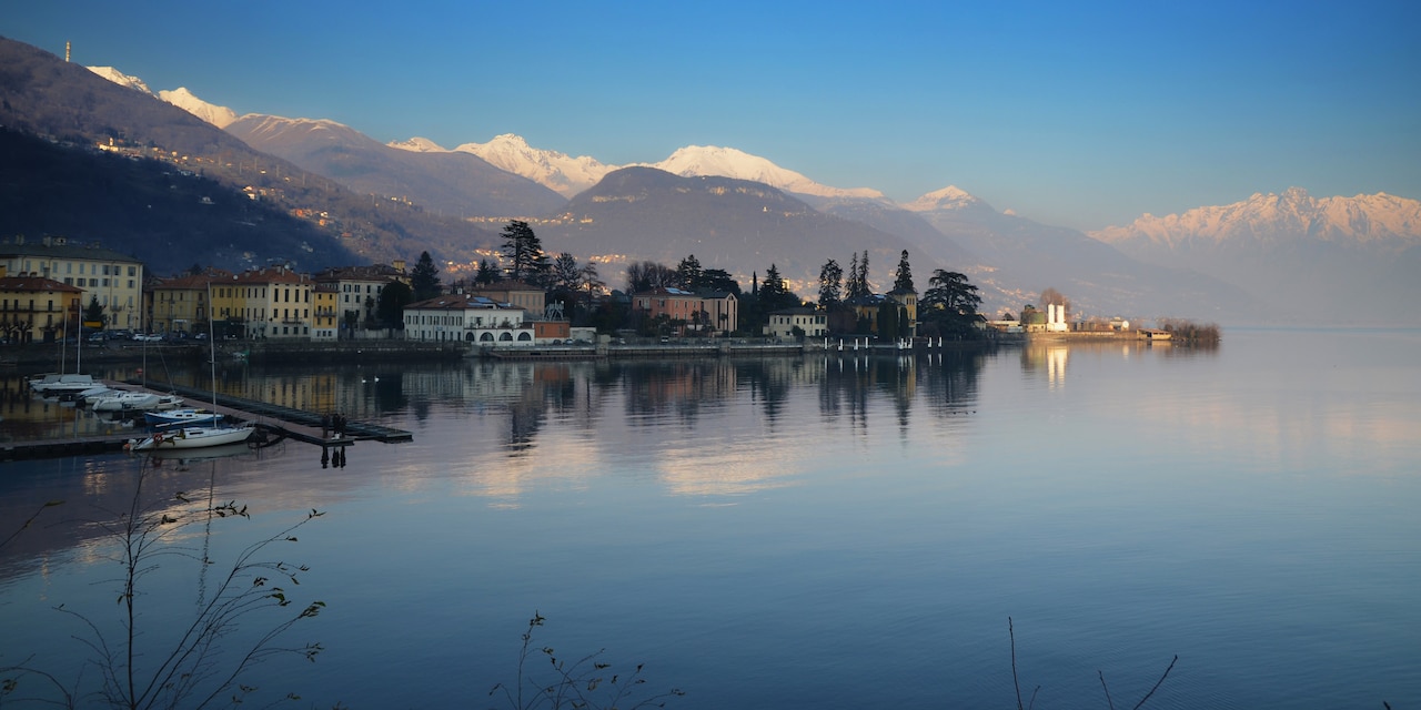 A calm lake reflecting clouds is surrounded by villas and mountains A calm lake reflecting clouds is surrounded by villas and mountains