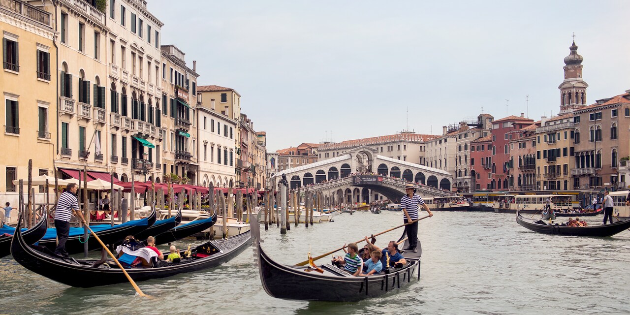 Gondoliers steer several gondolas filled with people on a canal in Venice, Italy Gondoliers steer several gondolas filled with people on a canal in Venice, Italy