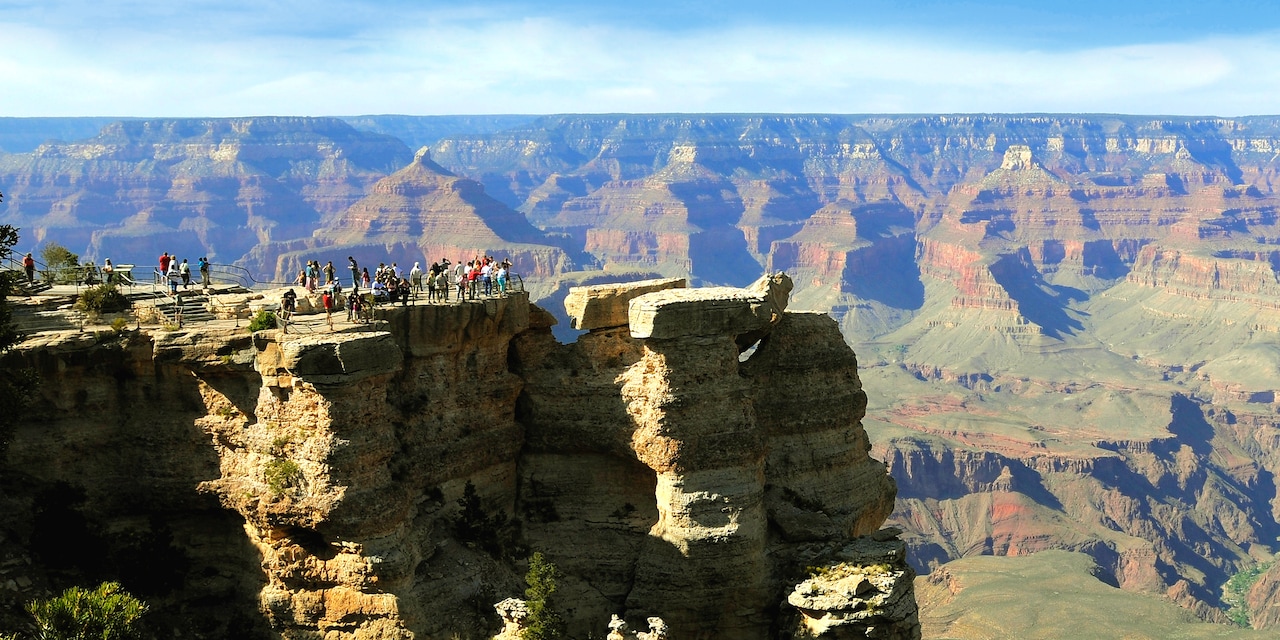 People stand atop a tall mesa viewing the Grand Canyon People stand atop a tall mesa viewing the Grand Canyon