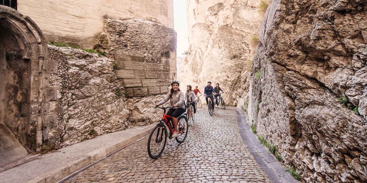 A group of people ride bicycles on a cobblestone street that is lined with large stone buildings