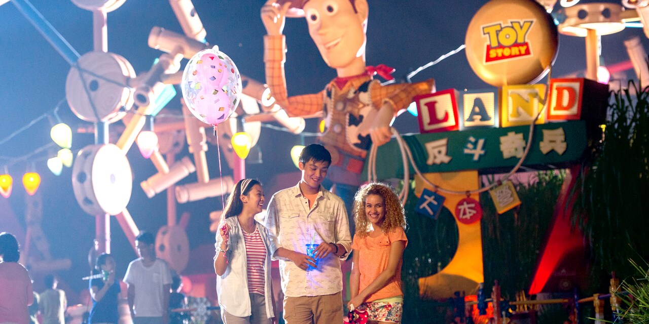 Two teenage girls and a teenage boy stand in front of a Sheriff Woody figure at the entrance to Toy Story Land at Hong Kong Disneyland