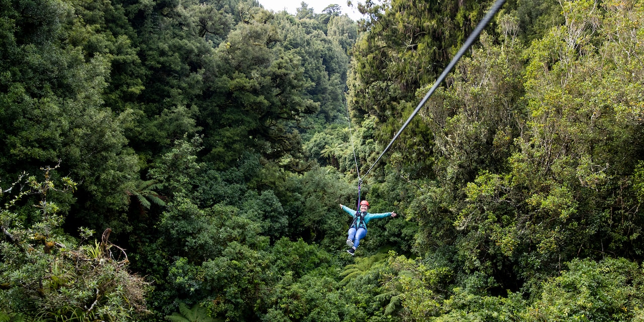 A person zip lines through tree tops with their arms outstretched