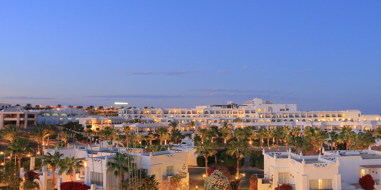 A panoramic view of the Coral Sea Sensatori Resort buildings on palm tree lined roads lit up at dusk A panoramic view of the Coral Sea Sensatori Resort buildings on palm tree lined roads lit up at dusk