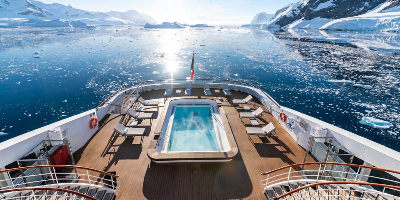 A pool with steam rising from the water at the front of a ship overlooking glaciers in Antarctica