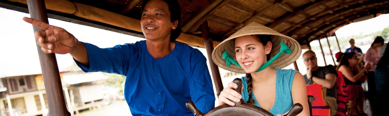 The driver of a roofed touring boat cruising on a river lets a female tourist take the wheel The driver of a roofed touring boat cruising on a river lets a female tourist take the wheel
