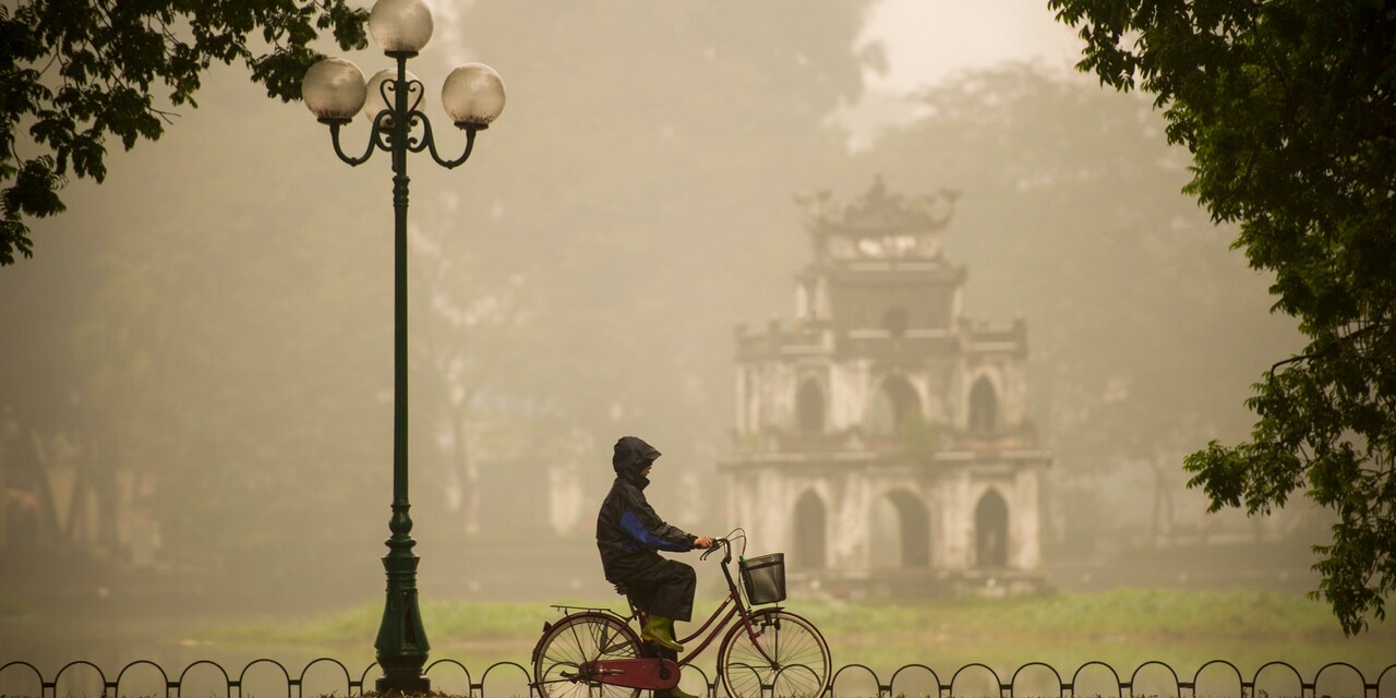 A hooded bicyclist rides past a lamp post on a sidewalk near an old temple in the rain
A hooded bicyclist rides past a lamp post on a sidewalk near an old temple in the rain