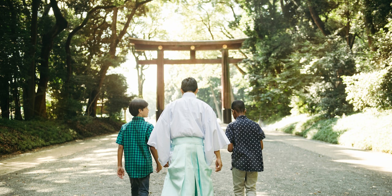 Two boys and a monk walk down a path towards a tojii gate at Meiji Shrine Two boys and a monk walk down a path towards a tojii gate at Meiji Shrine