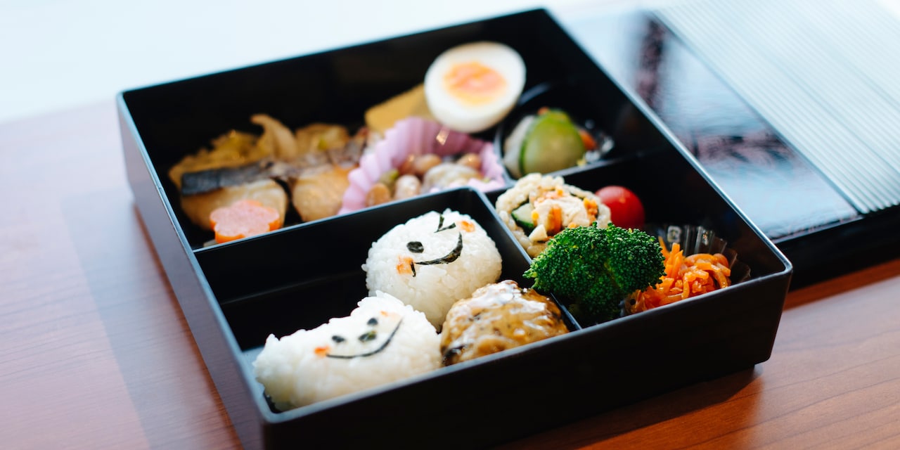 A Japanese bento box filled with various food, including rice balls with seaweed faces