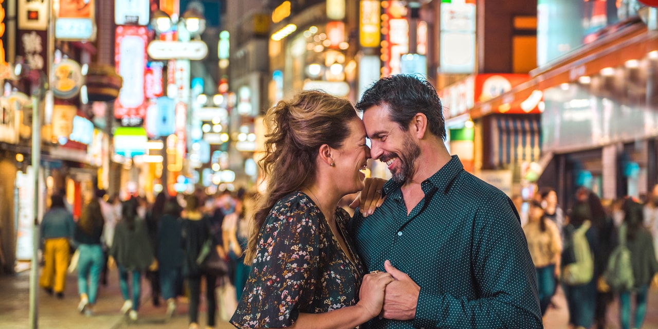 A couple hold hands while sharing a romantic moment on a neon-lit Tokyo street at night A couple hold hands while sharing a romantic moment on a neon-lit Tokyo street at night