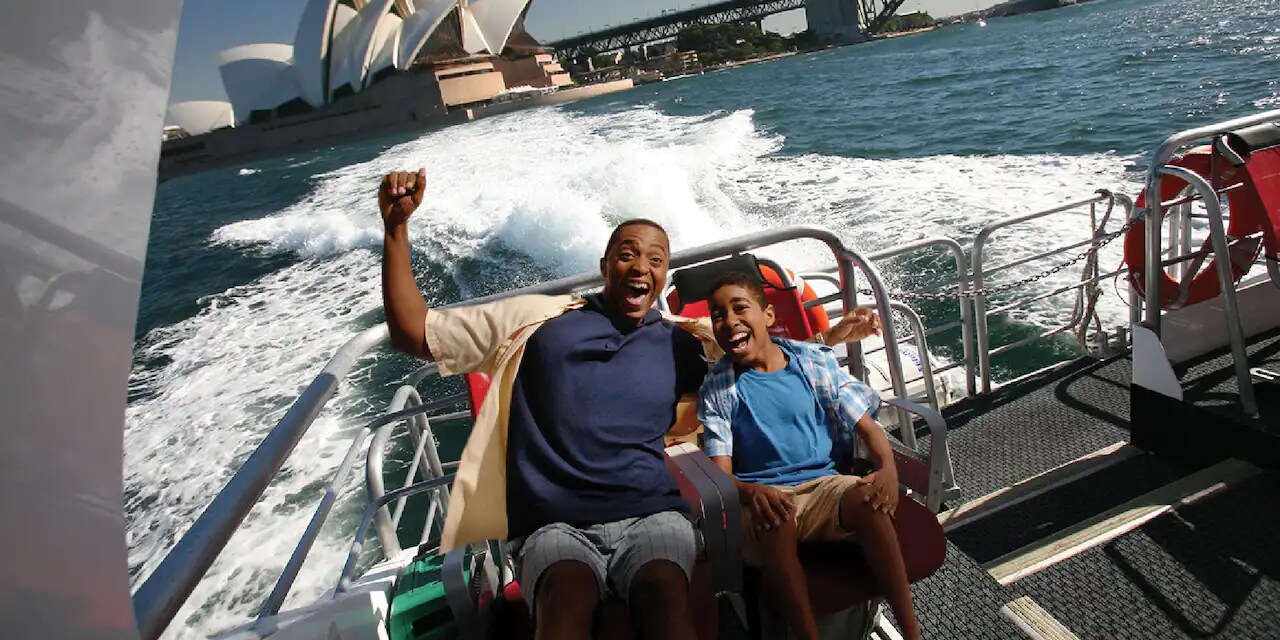 A man and a boy ride a speed boat through Sydney Harbour near the Sydney Opera House