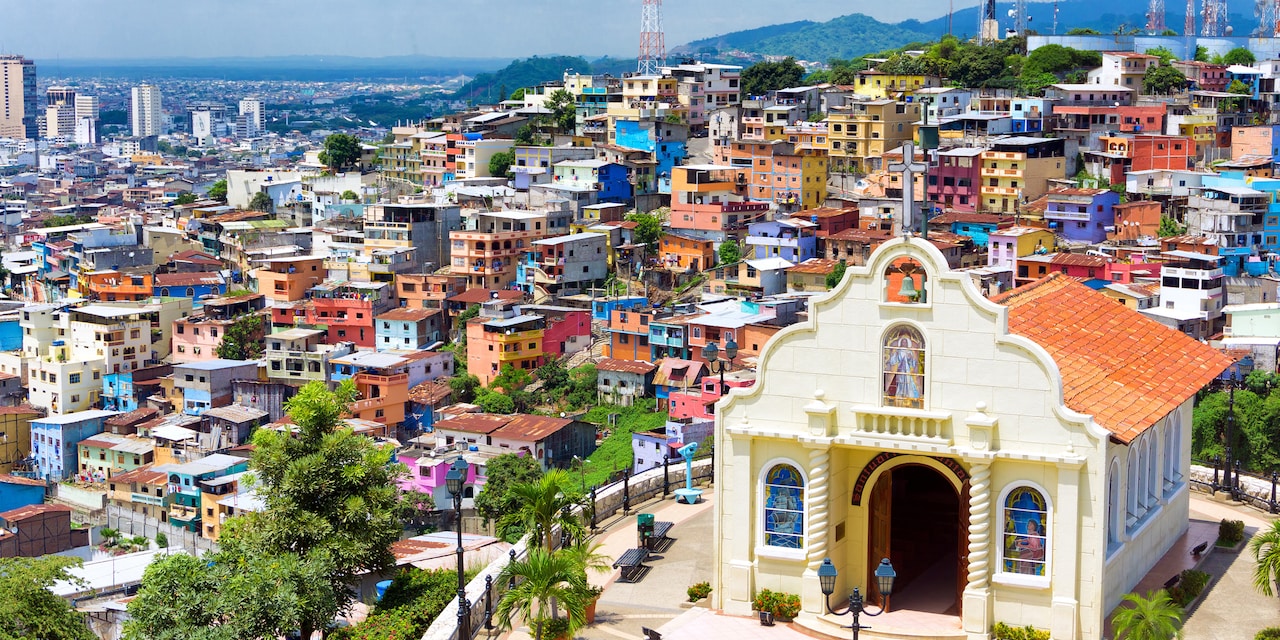 A church sits atop a hill overlooking the tiered buildings of Guayaquil, Ecuador that is spread out to the city skyline and a backdrop of mountains in the distance A church sits atop a hill overlooking the tiered buildings of Guayaquil, Ecuador that is spread out to the city skyline and a backdrop of mountains in the distance