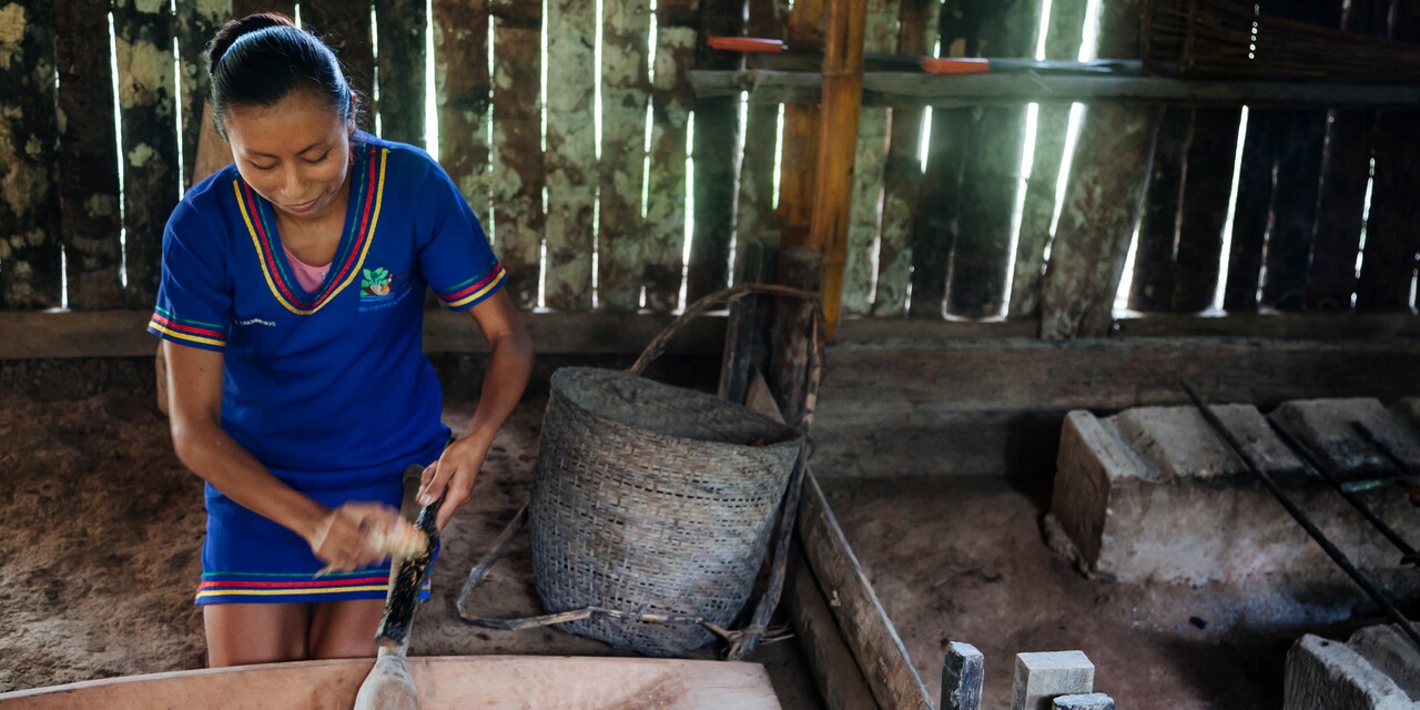 A Kichwa woman prepares food with traditional tribal tools including a canoe shaped dish in a room with a dirt floor A Kichwa woman prepares food with traditional tribal tools including a canoe shaped dish in a room with a dirt floor