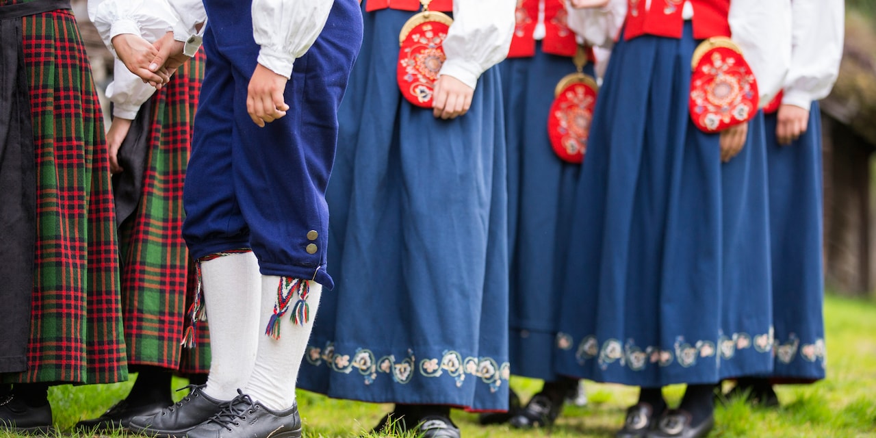 A group of Norwegian men and women, dressed in traditional costumes, are seen from the waist down