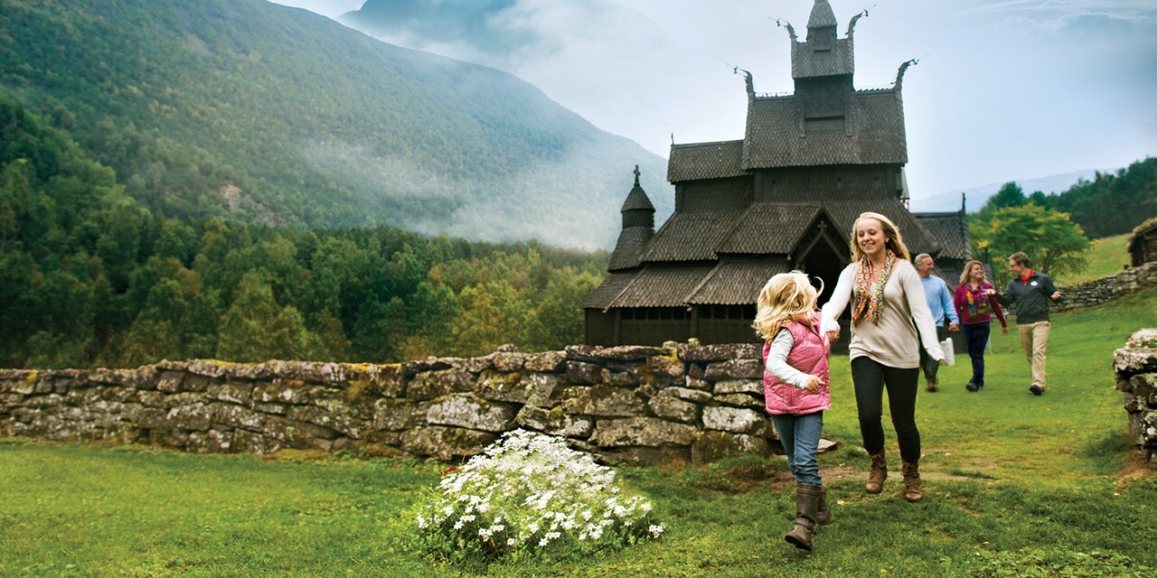 2 girls, their parents and an Adventure Guide walk in the field outside a stave church 