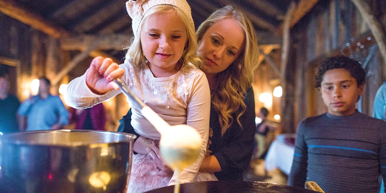 A mother holds her daughter who ladles batter onto a grill