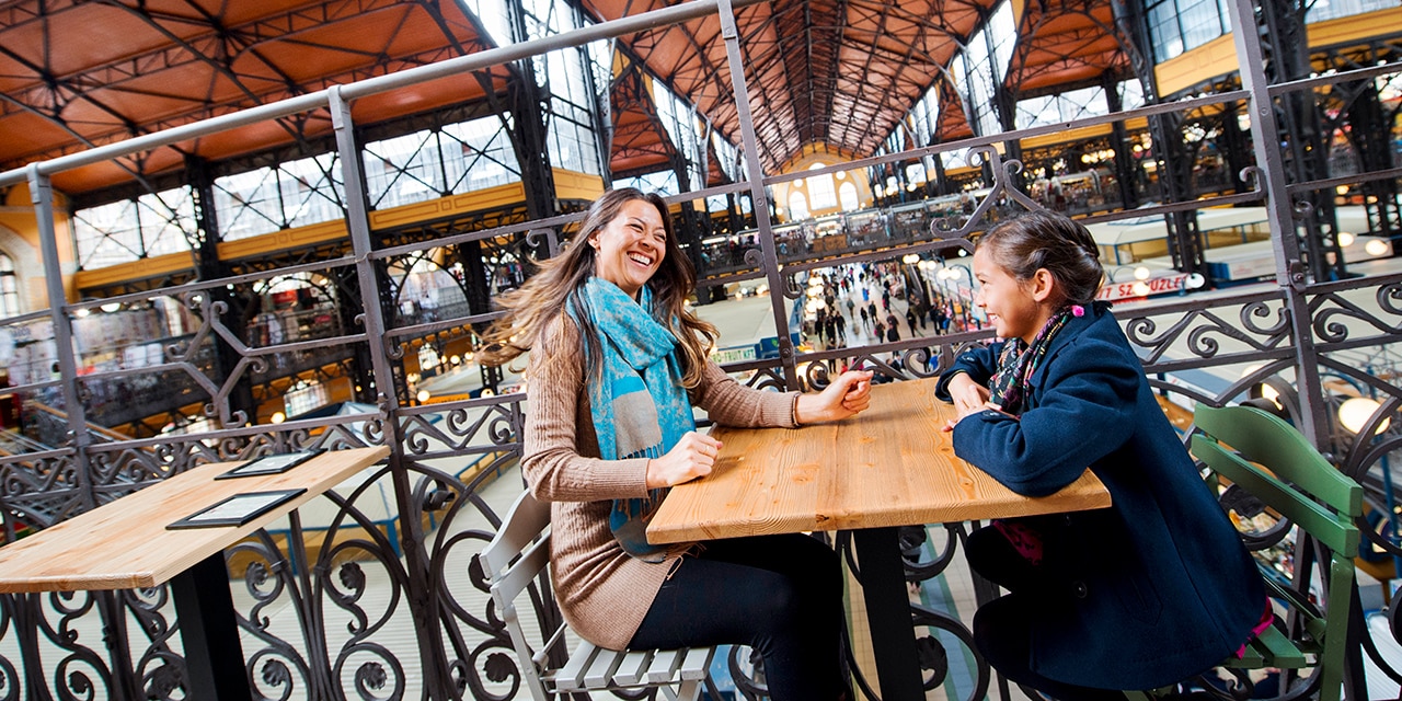 A mother and daughter sit at a table and share a laugh in Budapest’s Great Market Hall A mother and daughter sit at a table and share a laugh in Budapest’s Great Market Hall