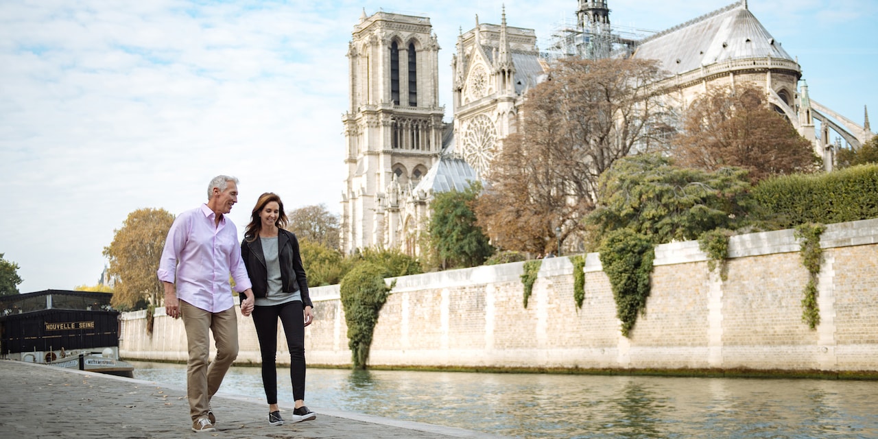 A couple hold hands as they walk along the Seine River near Notre Dame Cathedral in Paris, France A couple hold hands as they walk along the Seine River near Notre Dame Cathedral in Paris, France