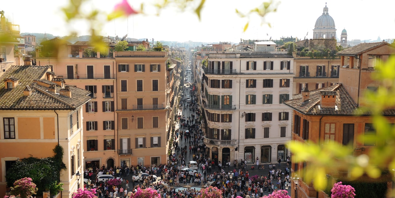 A rooftop view of a crowed street in Rome with a domed church in the distance A rooftop view of a crowed street in Rome with a domed church in the distance
