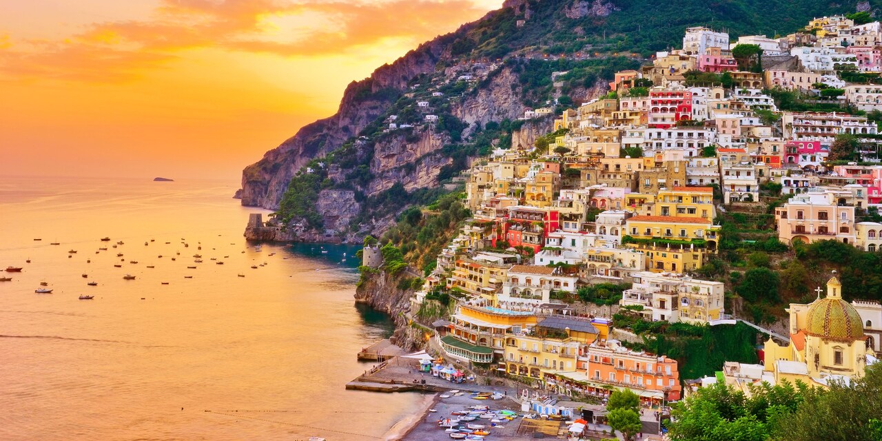 Colorful Positano houses stacked against the mountain with the reflection of the sunset on the sea