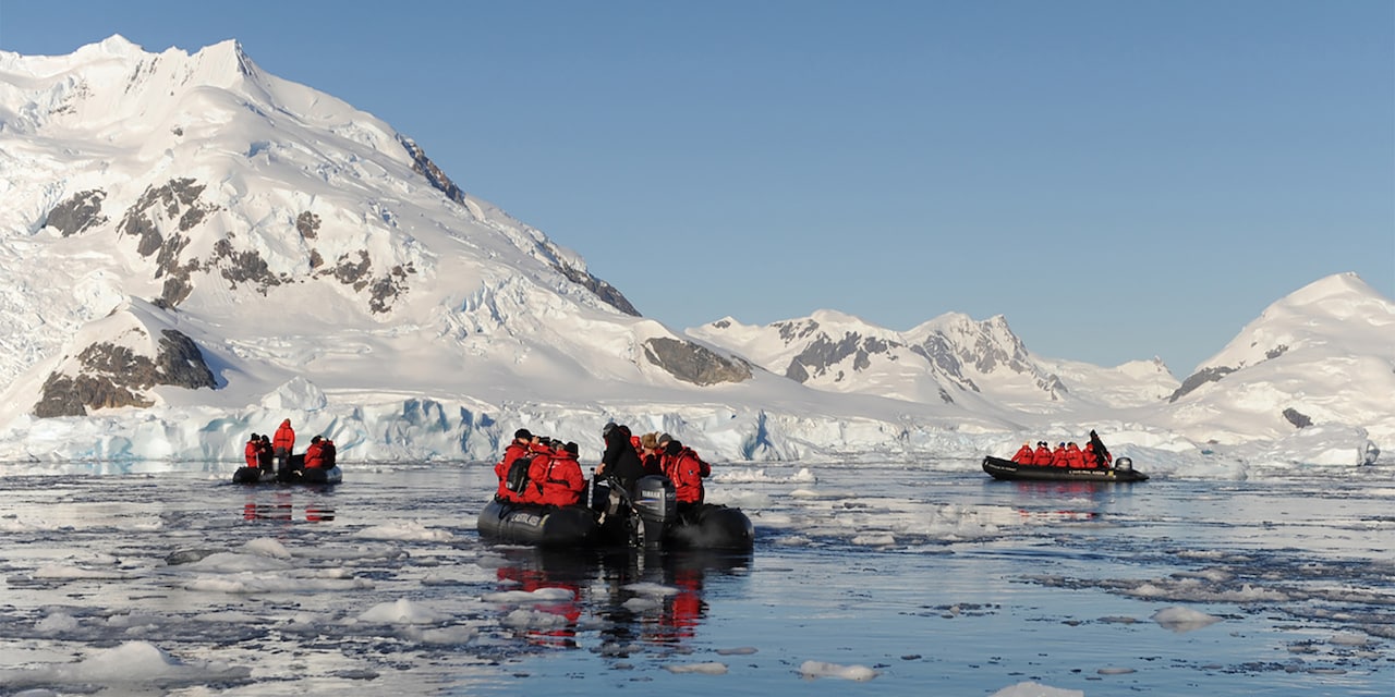 Several inflatable Zodiac boats filled with passengers cruise in the water near a glacier Several inflatable Zodiac boats filled with passengers cruise in the water near a glacier