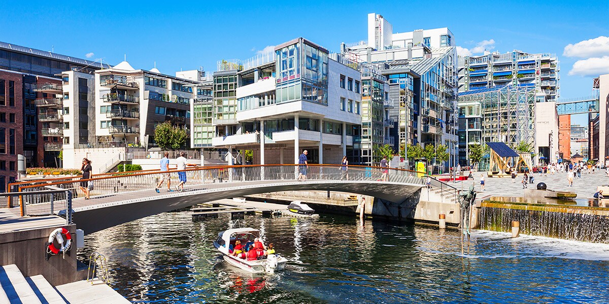 People walk across a bridge as a boat cruises below in the city of Oslo, Norway People walk across a bridge as a boat cruises below in the city of Oslo, Norway