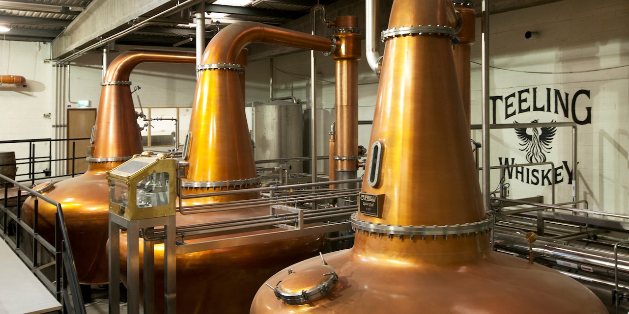 A row of distilling vats in front of a ‘Teeling Whiskey’ sign