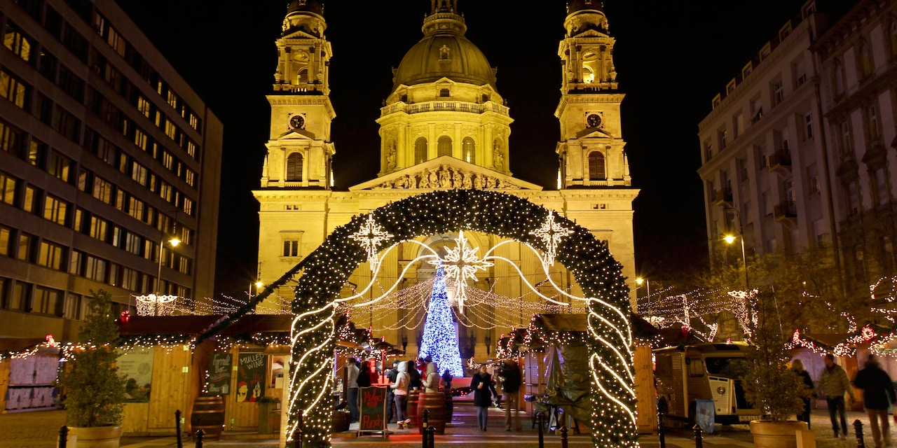 A Christmas Market in front of a church, with a lit Christmas tree and a holly archway
 
