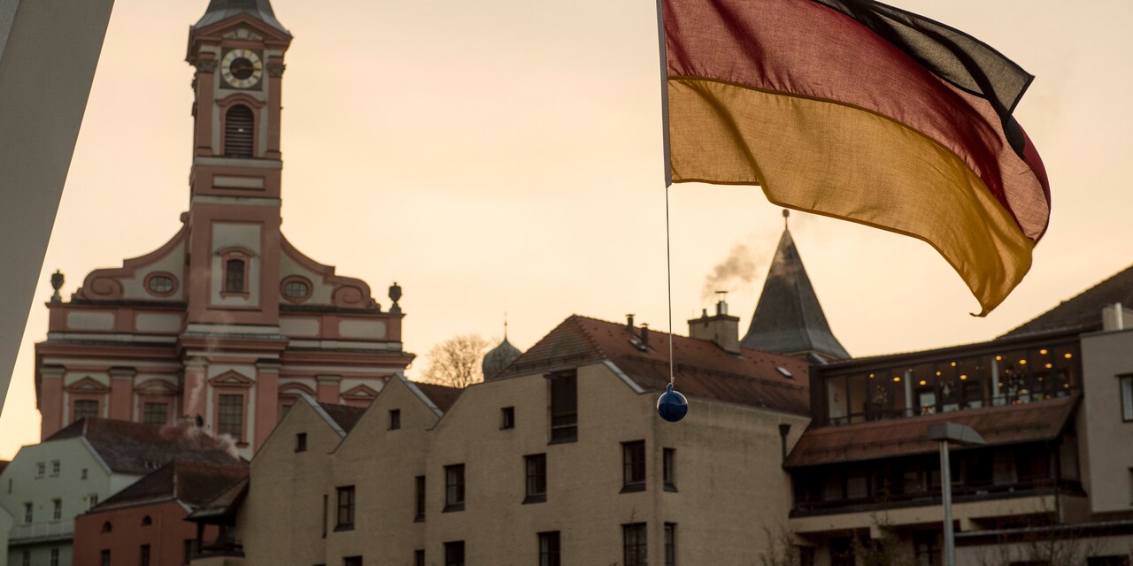 A German flag hangs near several buildings including a large clock tower