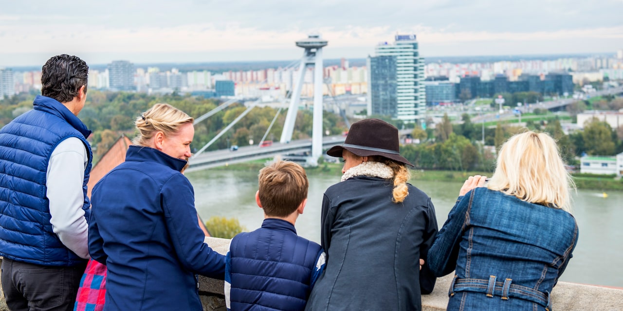 A family stands near a bridge and looks across a river at a modern city A family stands near a bridge and looks across a river at a modern city