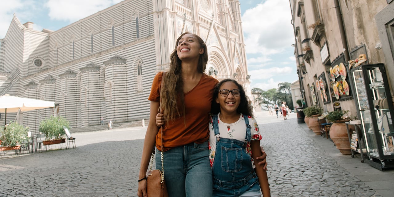 A mother and a daughter walk down a street arm in arm in Italy