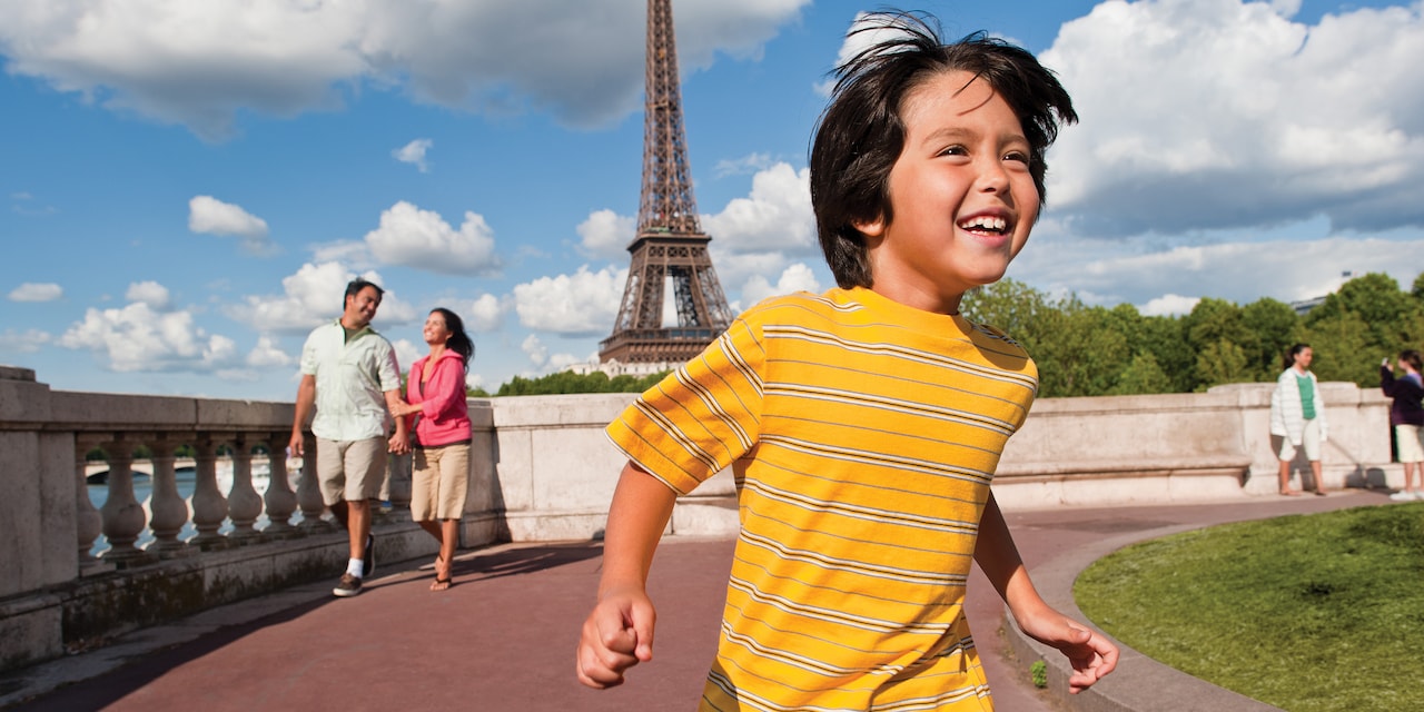 A young boy smiles as he runs along a path with the Eiffel Tower in the background