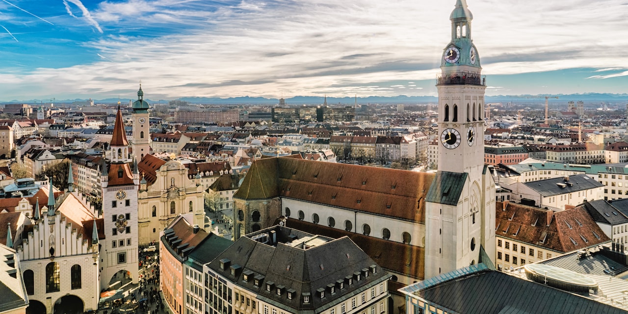 The city of Munich with a tall, spired clock tower standing against a bright, but cloudy sky