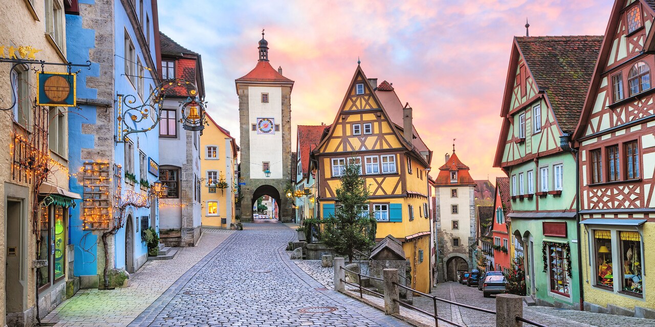 A cobblestone street runs through a quaint, shop lined street towards the clock tower in Rothenburg, Germany
