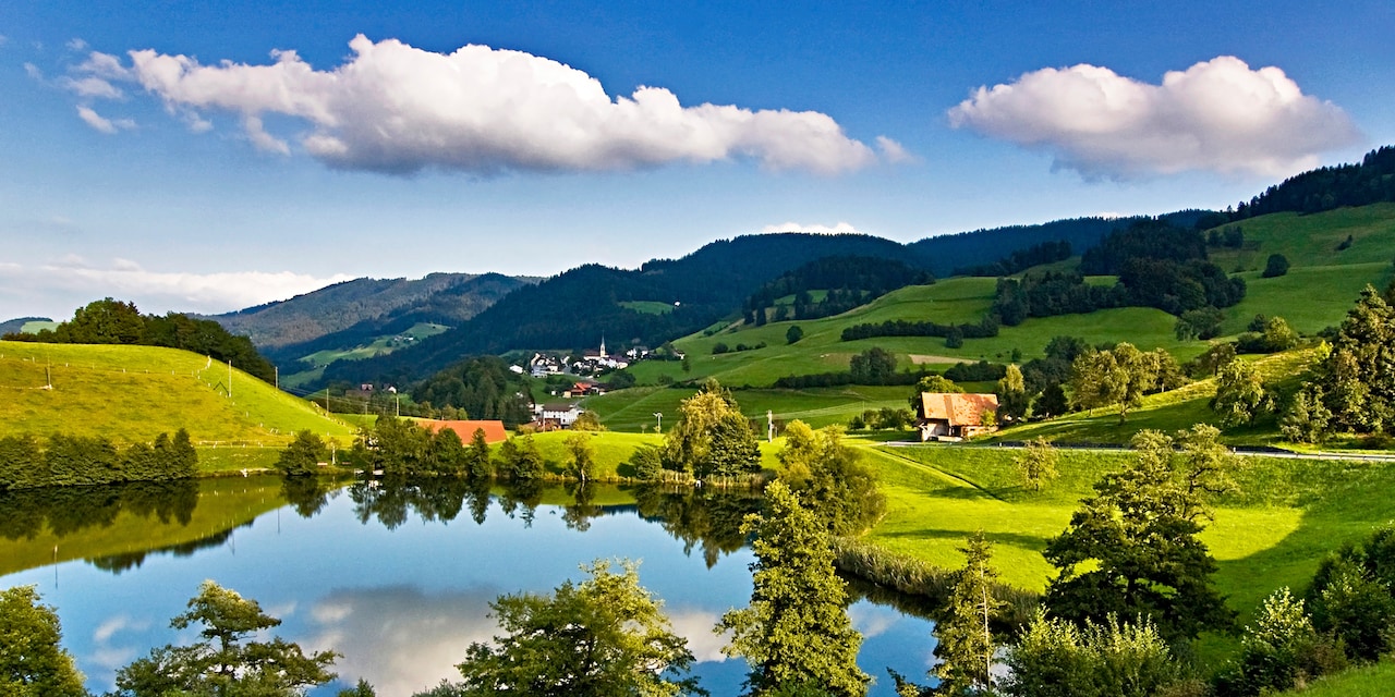 A farm near a lake and a village in a picturesque countryside with grass and rolling hills