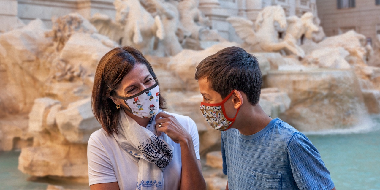 Mother and son wearing masks sitting in front of the Trevi Fountain in Rome Mother and son wearing masks sitting in front of the Trevi Fountain in Rome