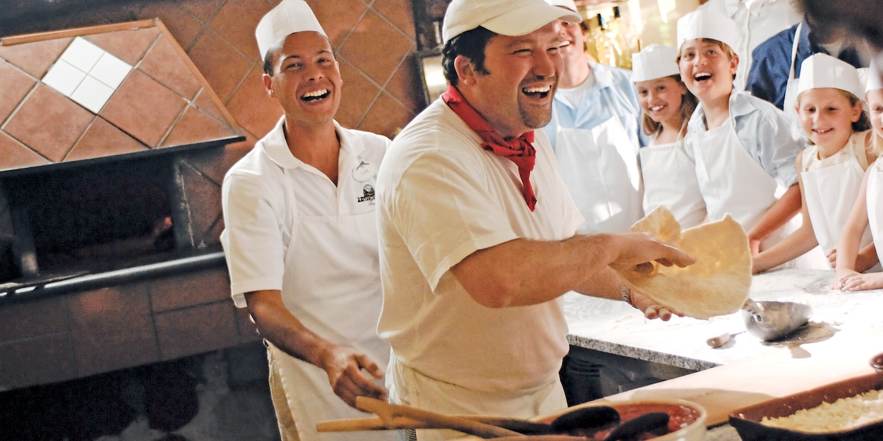 A smiling chef laughs while teaching a group of kids how to make pizza A smiling chef laughs while teaching a group of kids how to make pizza