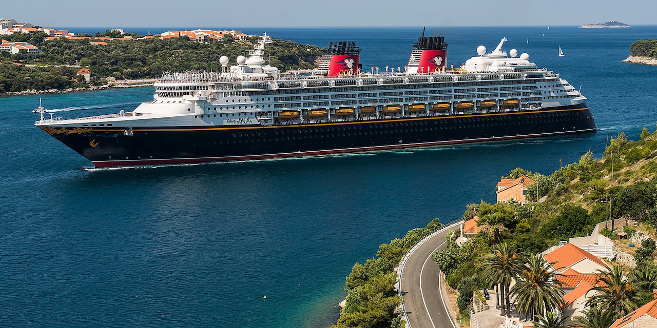 The Disney Magic Cruise Ship sails between two pieces of land with sail boats sailing in the distance The Disney Magic Cruise Ship sails between two pieces of land with sail boats sailing in the distance