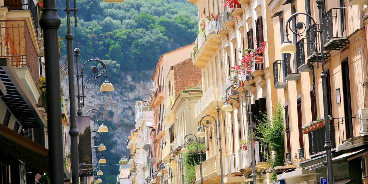 A row of buildings along a street lamp-lined avenue in Salerno, Italy lead to a verdant mountainside A row of buildings along a street lamp-lined avenue in Salerno, Italy lead to a verdant mountainside