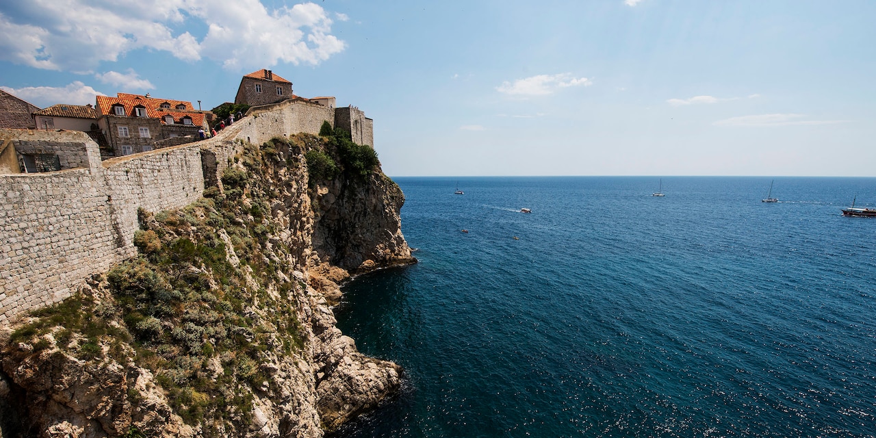 Buildings behind a stone wall sit atop a cliff overlooking the Adriatic Sea Buildings behind a stone wall sit atop a cliff overlooking the Adriatic Sea