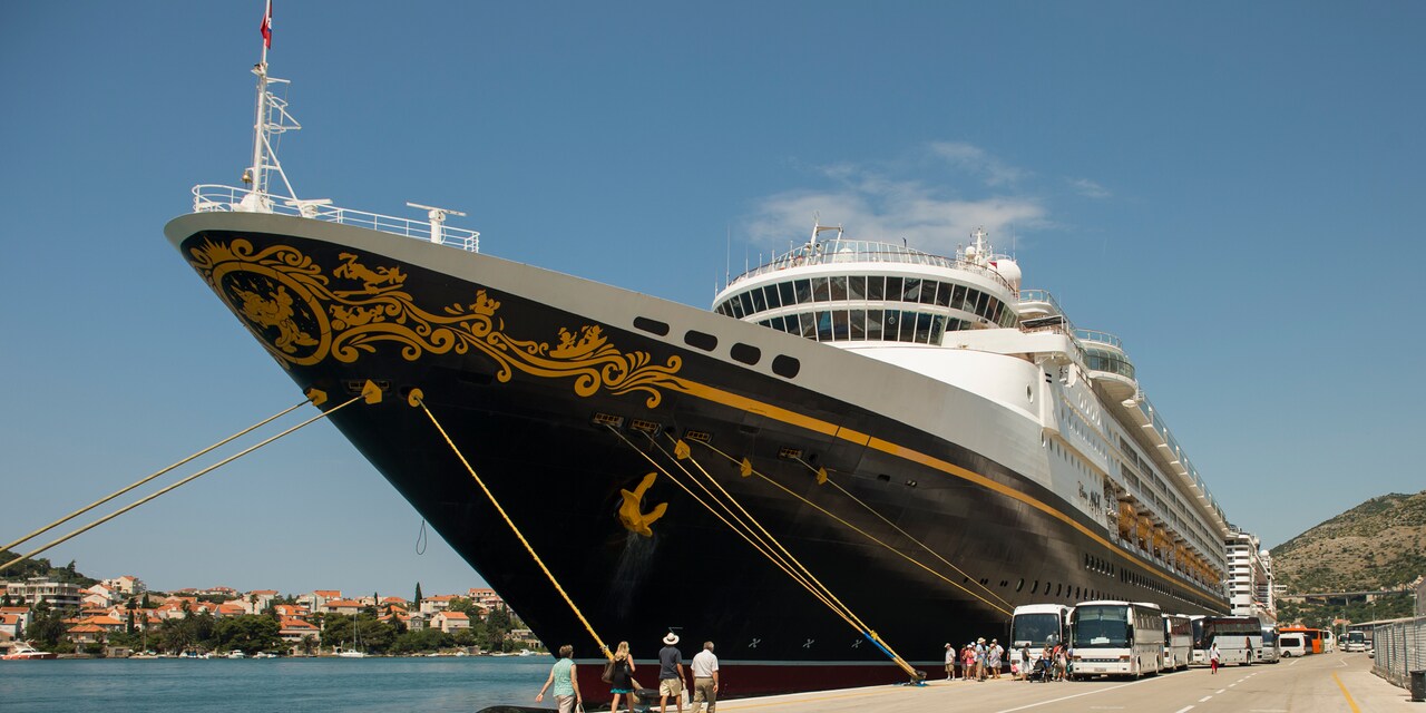 A family of 4 walks on a road towards a line of buses that are parked next to the Disney Magic cruise ship A family of 4 walks on a road towards a line of buses that are parked next to the Disney Magic cruise ship