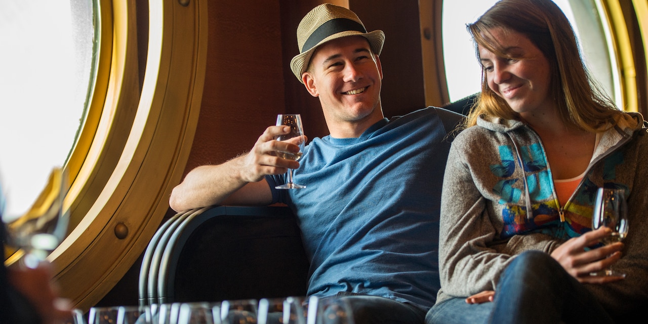 A man in a hat and woman drink cocktails onboard a ship A man in a hat and woman drink cocktails onboard a ship
